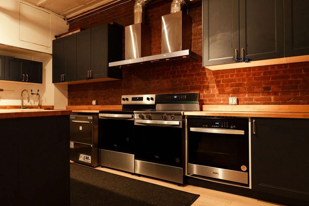 Two ranges, a vent hood and ovens along the brick wall