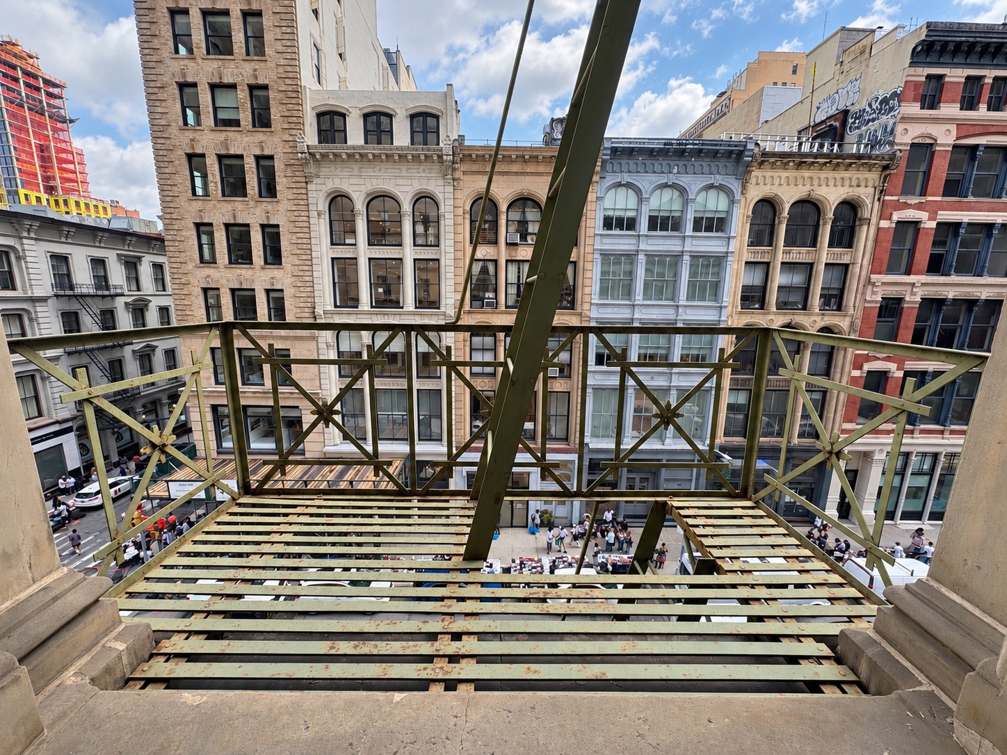 On the 4th-floor cast iron fire escape at 393 Broadway, looking across Broadway at 19th-century facades