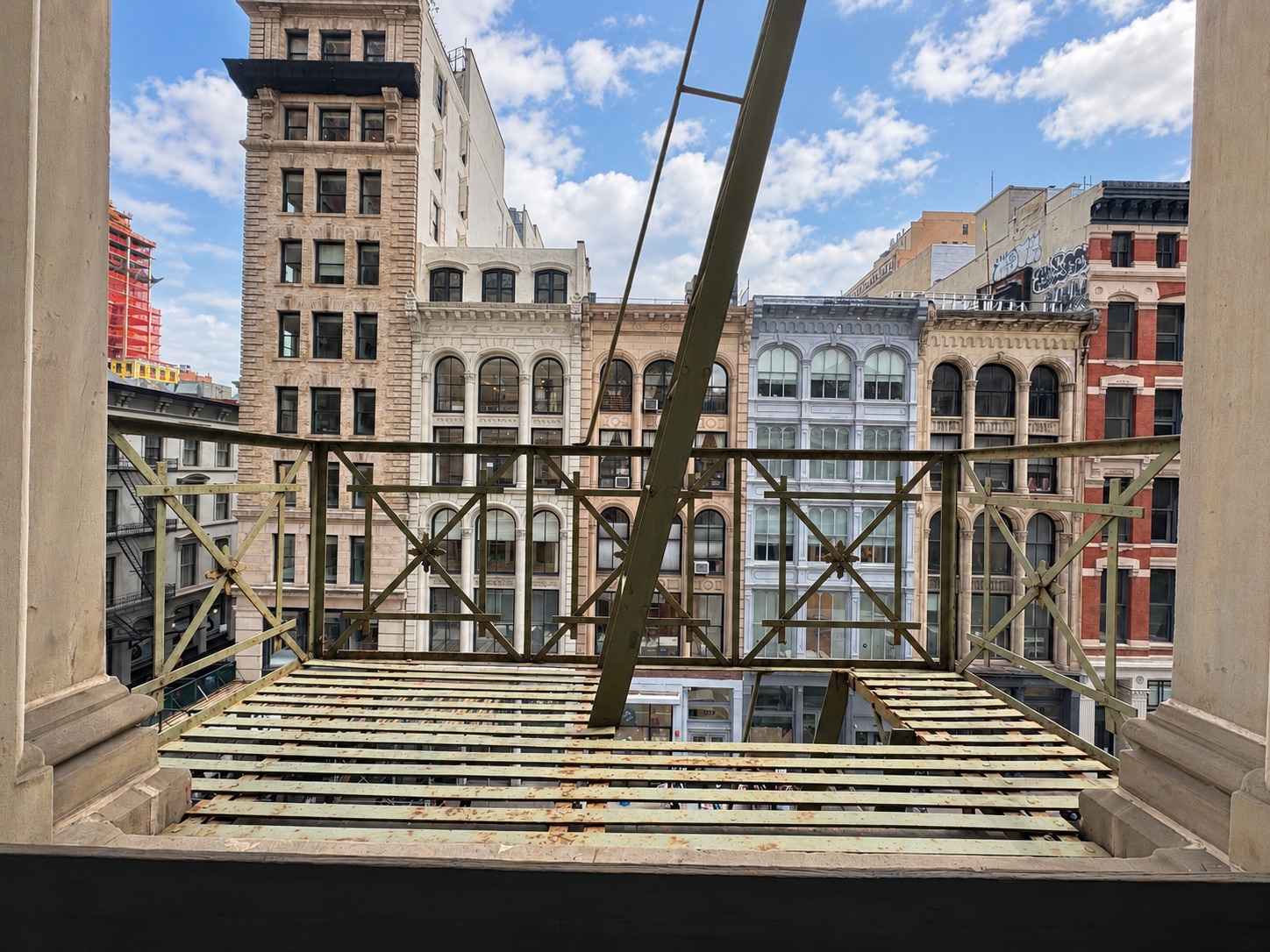 Gold-painted fire escape railings and ladder over Broadway, cast iron buildings across the street