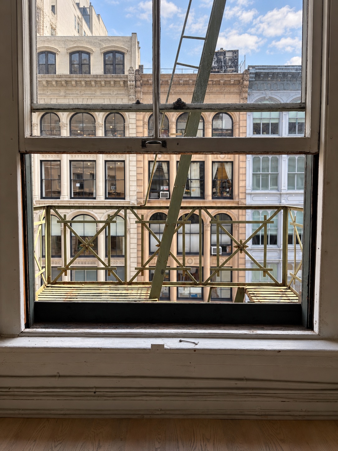 Tall loft window framing the fire escape ladder and the Broadway facades