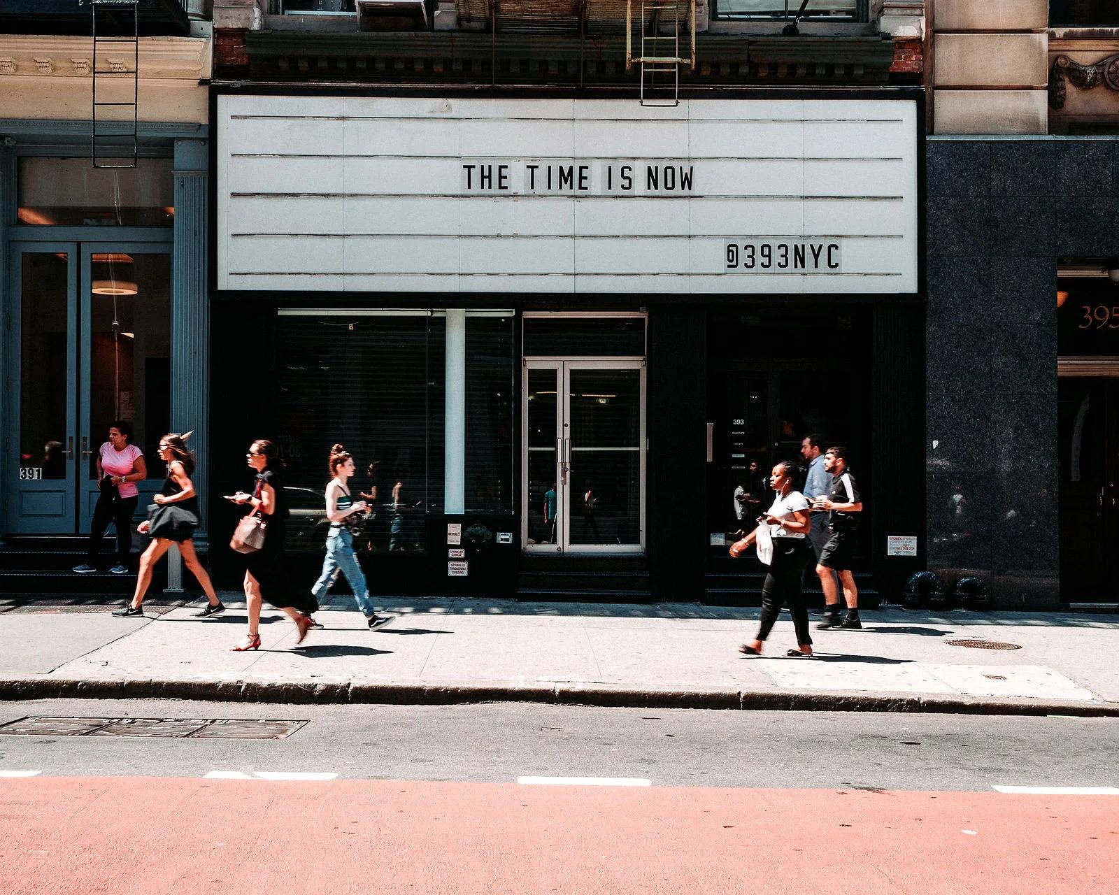 Lit marquee over the glass storefront with pedestrians passing on Broadway