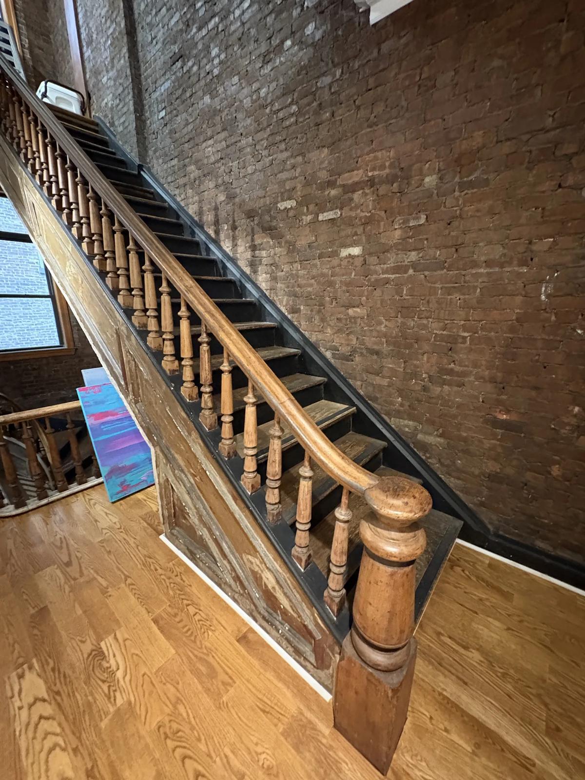 Original wood staircase with turned balusters and a newel post against exposed brick