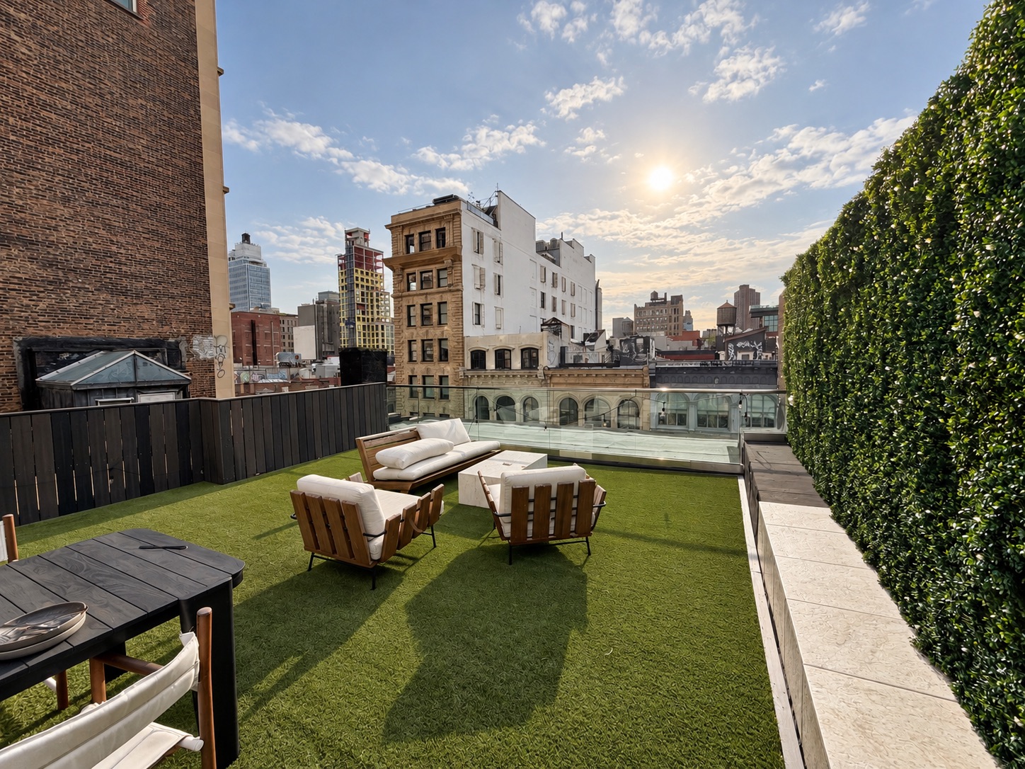 Tribeca penthouse roof deck with turf, lounge set, hedge wall and glass rail facing the skyline