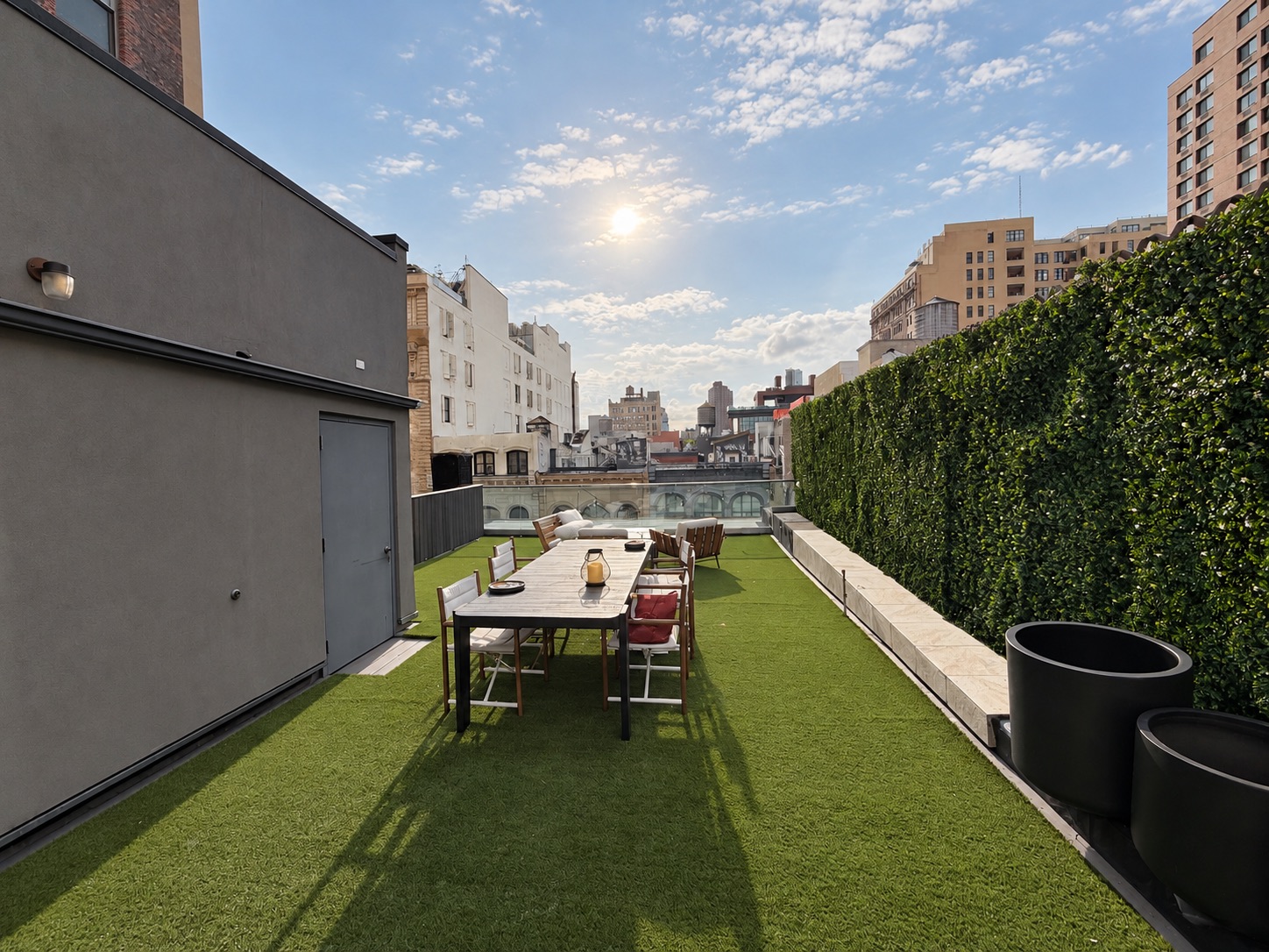 Long dining table on the turf deck between the penthouse wall and the hedge wall